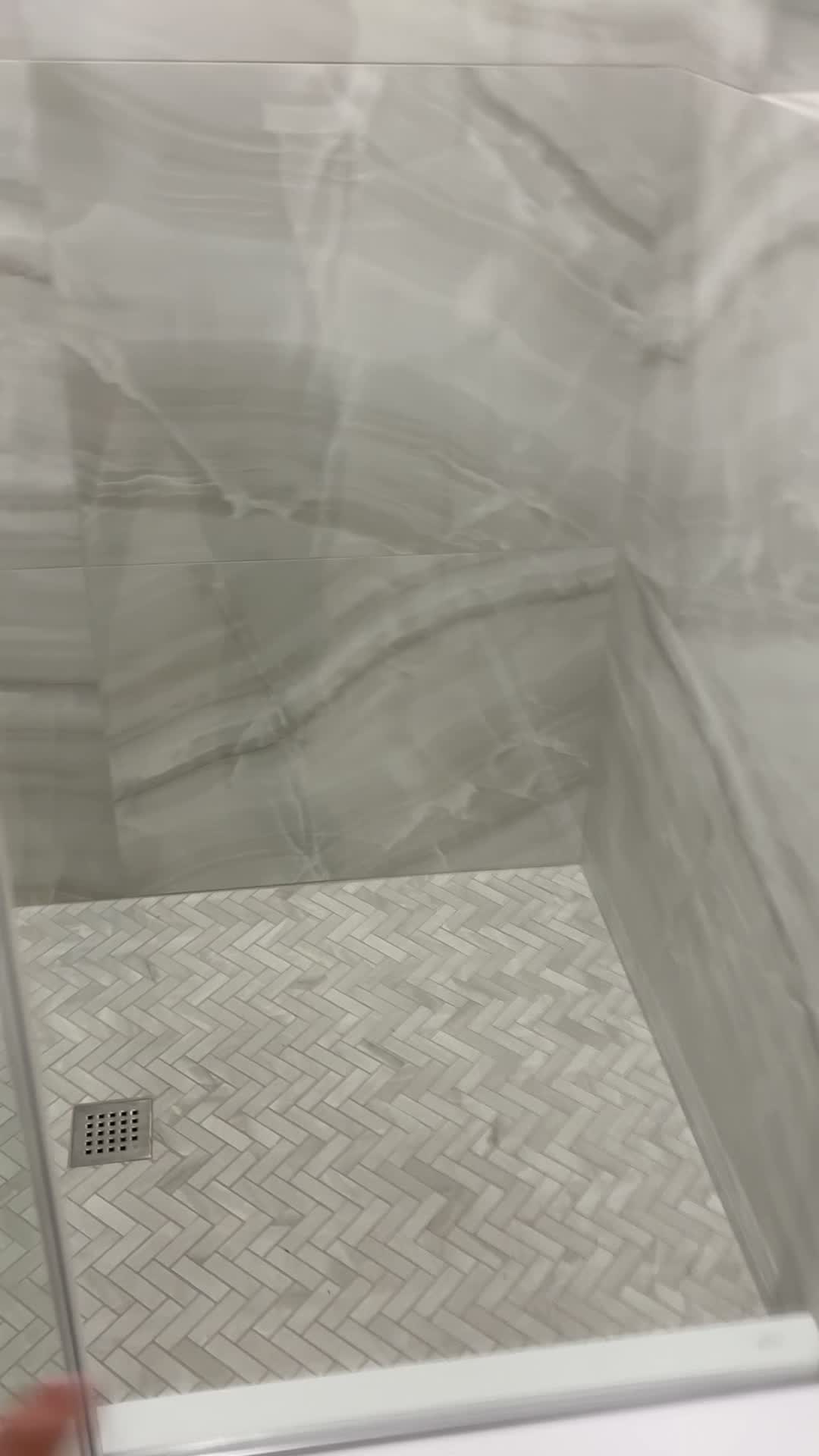 Herringbone mosaic shower floor with a square drain and marble-look tile walls