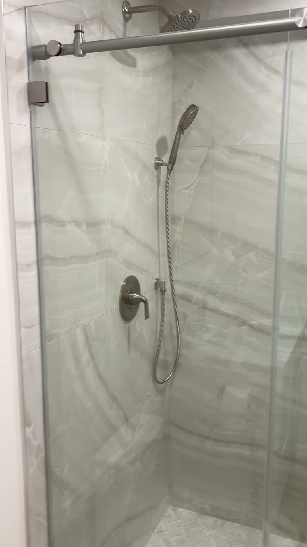 Finished shower with large marble-look tile walls, a sliding glass door and a handheld shower