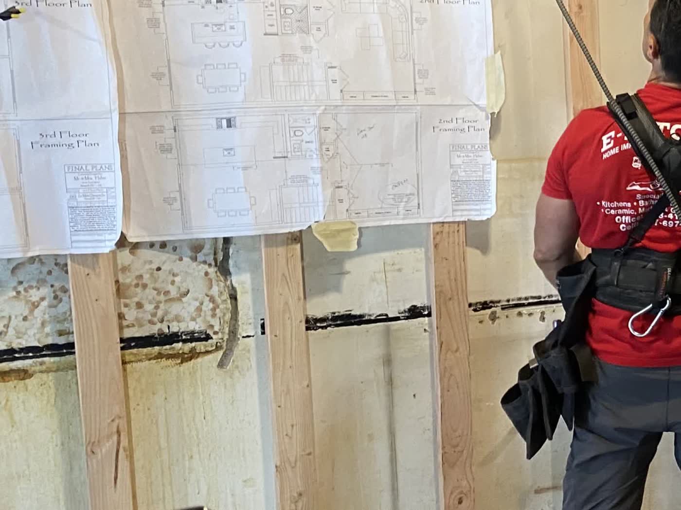 Floor plans taped to exposed framing during a gut renovation, with an E-Z Touch crew member alongside