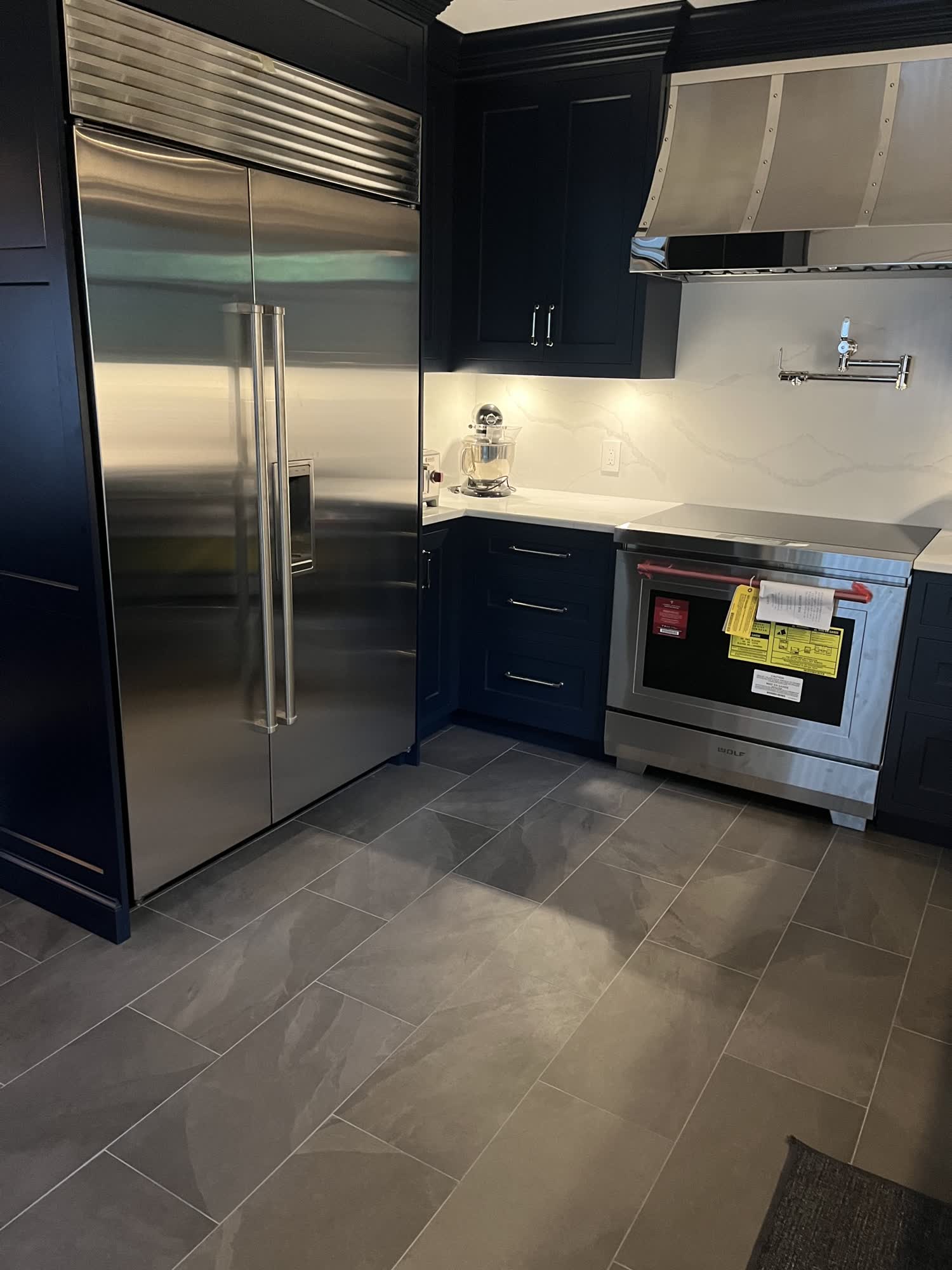 Finished navy blue kitchen with built-in stainless refrigerator, Wolf range and custom stainless hood