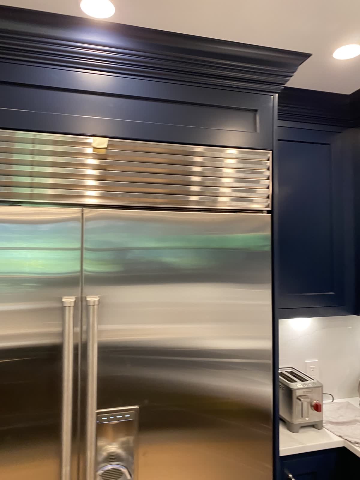 Built-in refrigerator trimmed flush into navy cabinetry with crown molding above