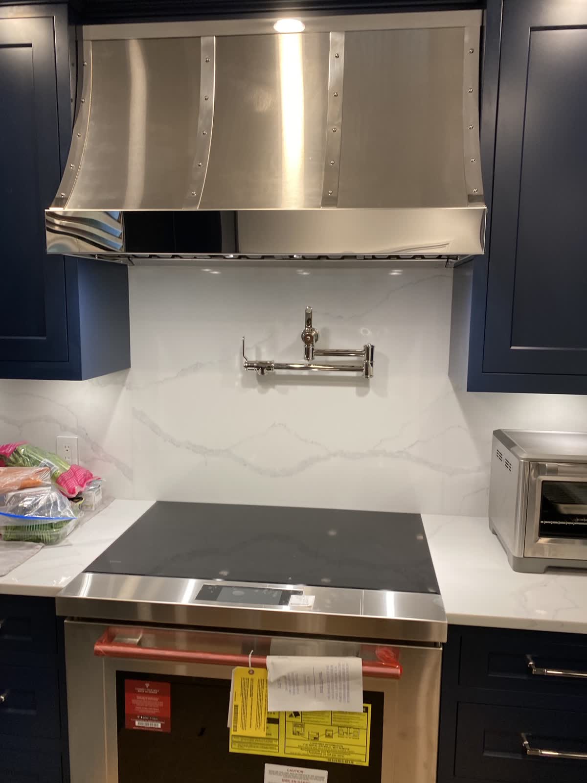 Custom riveted stainless range hood over a quartz backsplash with a pot filler