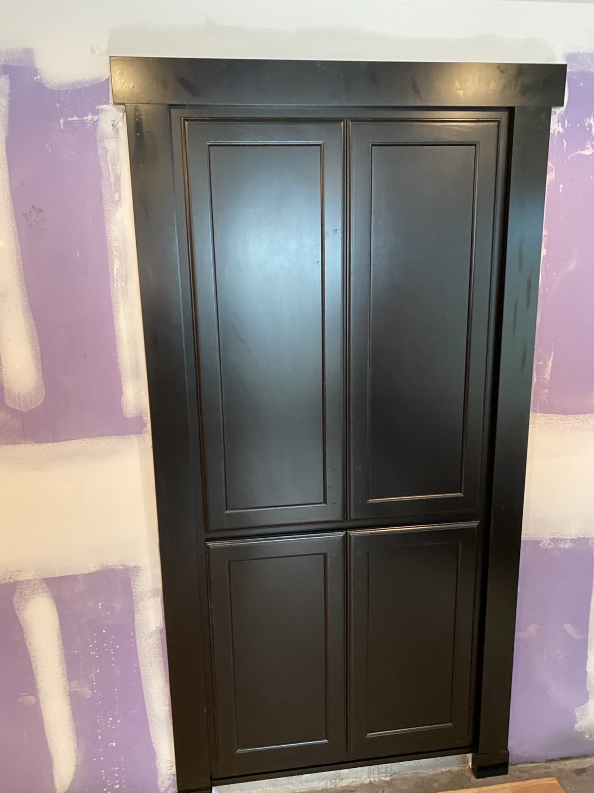 Custom dark painted built-in pantry installed against unfinished walls