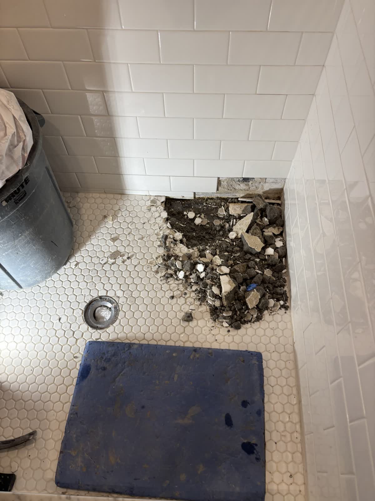Old hex tile shower floor being broken out, with the drain exposed