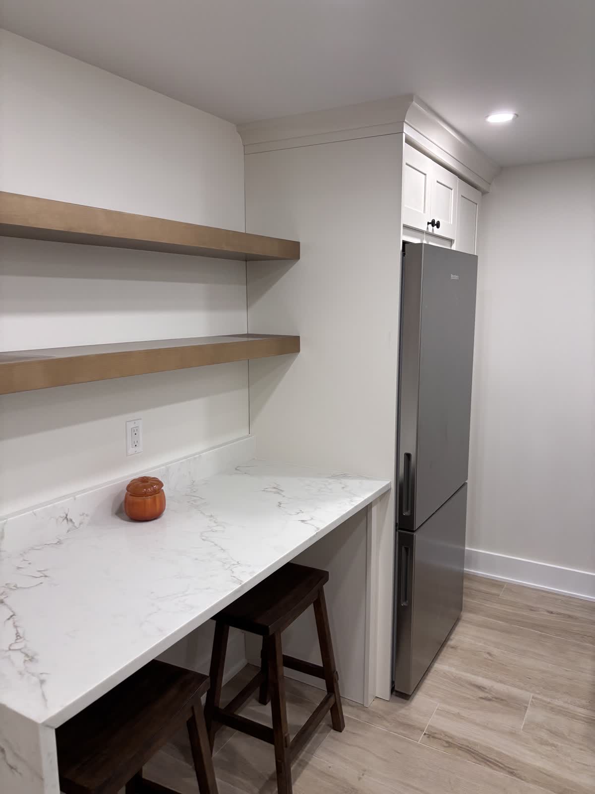 Floating wood shelves over a waterfall stone breakfast counter with stools