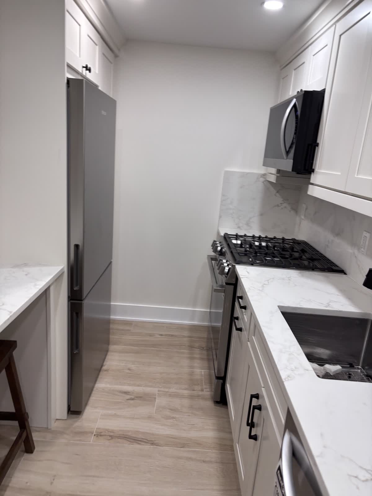Finished galley kitchen with white shaker cabinets and stainless appliances