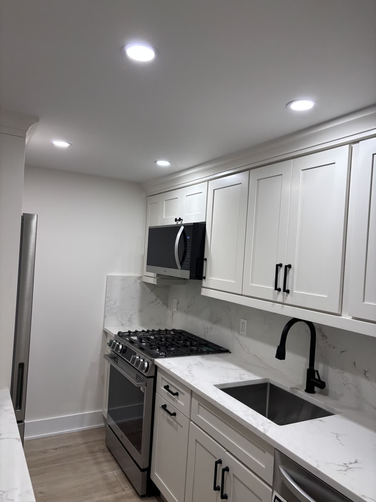 Finished white shaker kitchen with marble-look counters and backsplash, black hardware and a gas range